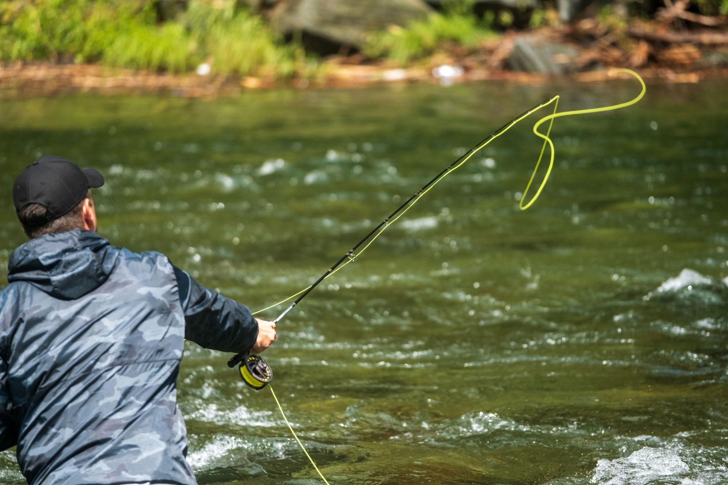 fisherman fly casting a bright yellow line over a fast flowing river
